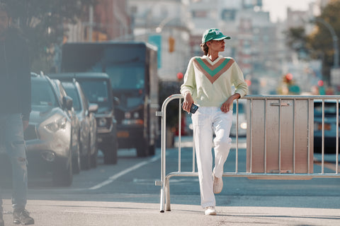 Model in the street wearing the Maya sweater with the white city pants and the LOVE Kap in green