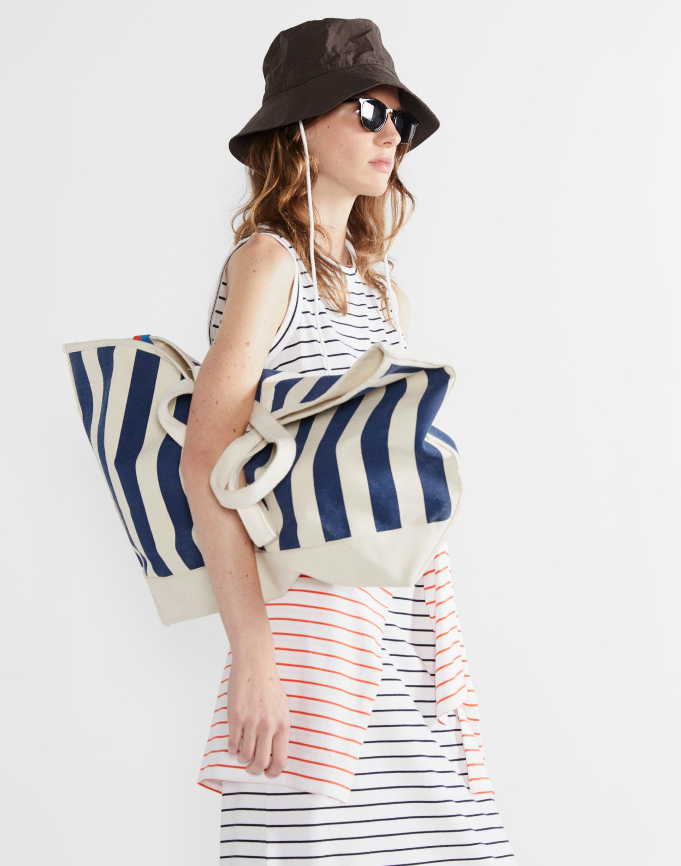 Model wearing The Tank Dress - White/Navy Pinstripe while holding a striped tote