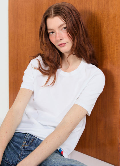 Model sitting against a wooden wall wearing The Modern - White