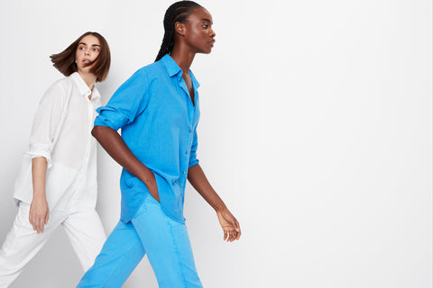 Two female models both wearing the Blanca shirt with the city pants, one wearing an all white set, the other wearing an all blue set. 
