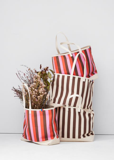 Still life of the over the shoulder all over striped totes in both canvas/walnut and in pink/poppy/walnut
